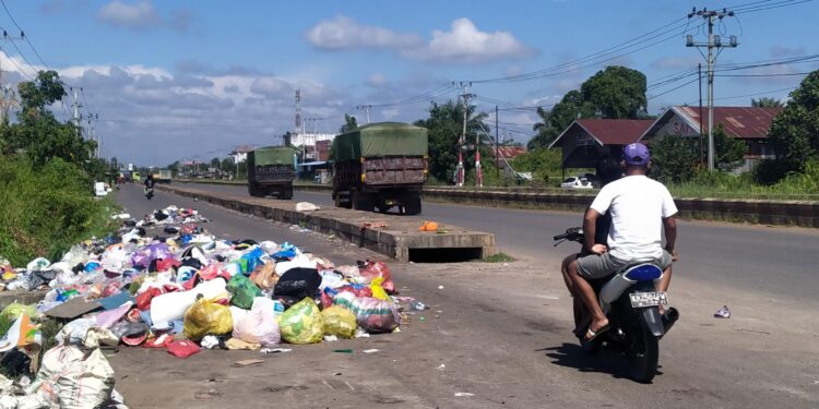 FOTO : AGUS/MATA KALTENG - Salah seorang pengendara motor melintas di dekat tumpukan sampah yang hingga meluber ke jalan raya di salah satu TPS di jalan Cilik Riwut Km 4,5 Sampit, Jumat 29 Juli 2022.