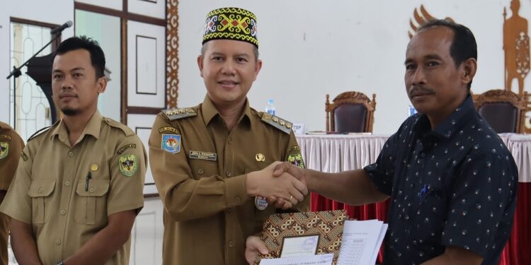 FOTO : DISKOMINFO SANTIK/MATA KALTENG - Bupati Gumas Jaya S Monong saat menyerahkan SK penetapan kebun plasma kepada Ketua Koperasi Dayak Hapakat Lipson, di GPU Damang Batu, belum lama ini.