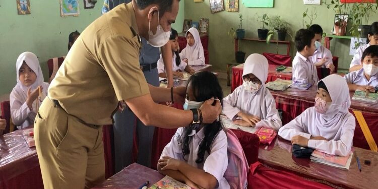 FOTO: RZL/MATAKALTENG - Camat Pahandut, Berlianto, saat memasangkan masker ke siswa.