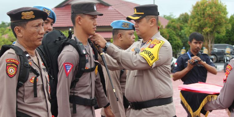 FOTO : HUMAS POLRES GUMAS/MATA KALTENG - Kapolres Gumas AKBP Theodorus Priyo Santosa menyematkan pita kepada perwakilan apel pergeseran pasukan pengamanan TPS pada Pilkada serentak tahun 2024, Jumat, 22 November 2024.