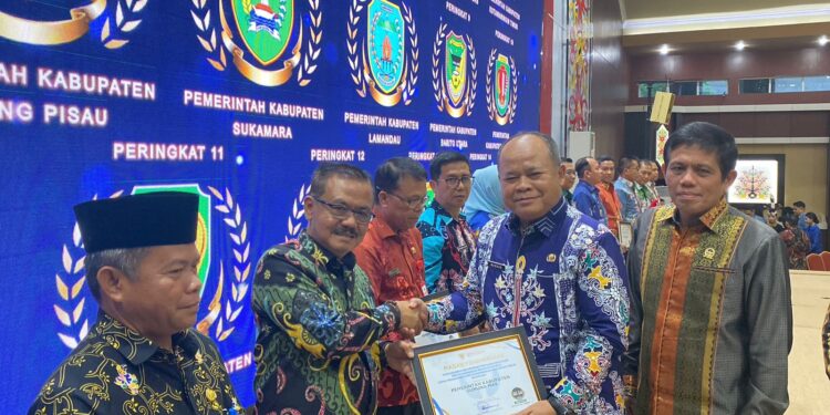FOTO : PROTOKOL GUMAS/MATA KALTENG - Plh Asisten Pemkesra Setda Provinsi Kalteng Maskur didampingi Anggota Ombudsman RI Jemsly Hutabarat, saat menyerahkan piagam penghargaan hasil survei kepatuhan pelayanan publik kepada Pj Bupati Gumas Herson B Aden, Jumat, 13 Desember 2024.